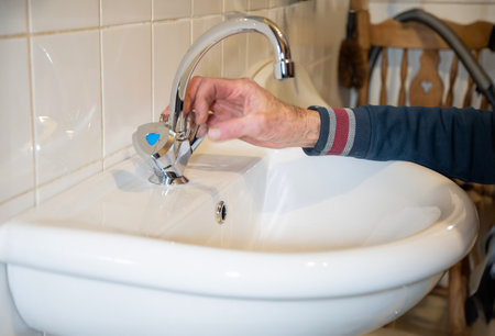 A man turns on a hot water tap in a sink, testing the operation of a newly installed plumbing system,の写真素材