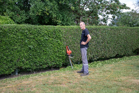 man standing in front of hedge trimmer stopped during work, gardener trimming hedge with electric hedge trimmer,の写真素材