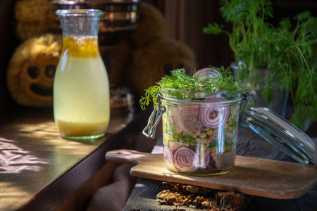 A jar of marinated herring with onions in mustard sauce with dill and green peas on a table in the...
