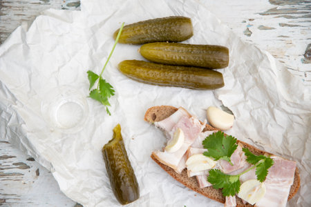 Rustic appetizer of pickles, rye bread with bacon, garlic and parsley on white paper, laid out on a weathered wooden surface,の写真素材