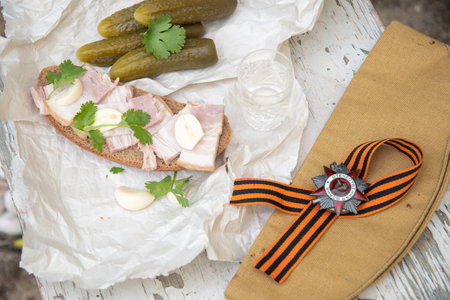 St. Georges ribbon, Order of the Great Patriotic War, holiday May 9, Victory Day, still life on a shabby chair with glass of vodka and a snack of lard with garlic and pickled cucumber,の写真素材
