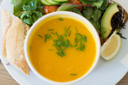 Yellow pumpkin soup with fresh herbs in a bowl, top view on a plate with fresh vegetable salad and pieces of white bread,の写真素材