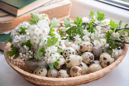 Arranging small quail eggs and white hawthorn flowers in a wicker basket, capturing the freshness of...