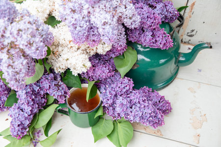 Green enamel mug and kettle nestled among vibrant purple and white lilac flowers on a rustic white...