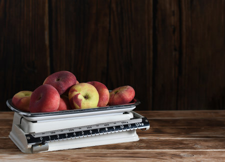Weighing ripe flat peaches on vintage metal kitchen scales on wooden background highlighting their rustic style and coziness,の写真素材
