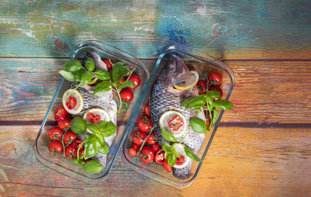 Two large dorado fish, tilapia, carp in a fireproof baking dish with cherry tomatoes, step by step cooking instructions, top view of the dish garnished with fresh basil,の写真素材