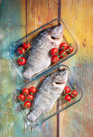 Fresh large dorado fish, tilapia, carp in baking dish with cherry tomatoes, step by step recipe instructions, top view on old green wooden tableの写真素材