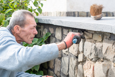 A builder carefully applies cement between the stones of a wall with a narrow trowel, restoring the appearance of a historic building using professional methods and toolsの写真素材