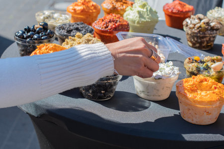 Womans hand picking up a sample of fresh tzatziki sauce from a variety of dips and spreads displayed on a table at an outdoor food market, offering a colorful and tempting selectionの写真素材