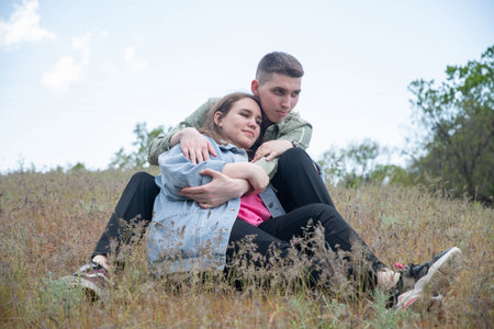 Young adults finding comfort in each others arms, sharing loving embrace while sitting together amidst dry grass, symbolizing close relationship, affection, and happiness outdoorsの写真素材
