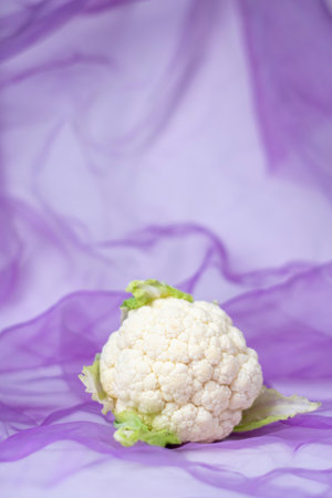Fresh, raw cauliflower presenting a healthy food option, placed on a draped purple sheer fabric background, highlighting natural beauty and wellness lifestyleの写真素材