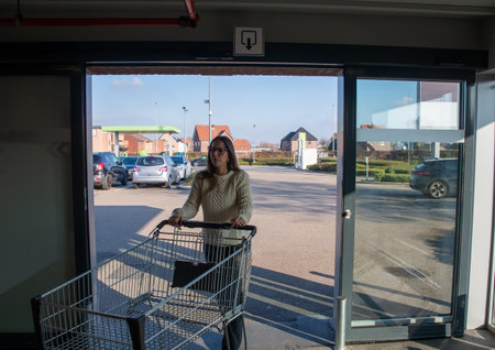 Woman standing with an empty shopping cart, pushing it from inside a supermarket, moving through an...