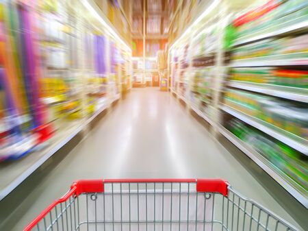 Supermarket aisle with empty red shopping cartの写真素材