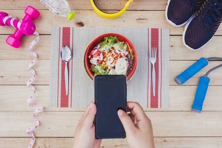 Female hands holding phone and fitness equipment on the floor.