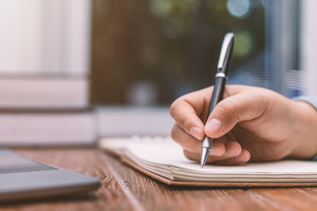 woman holding a pen sitting on a desk writingの写真素材