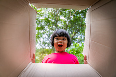 Happy asian little girl opening a cardboard box in the park.の写真素材