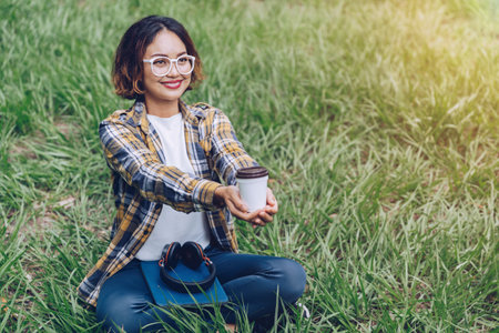 Asian woman sitting and drinking coffee in the gardenの写真素材
