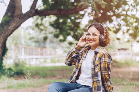 Asian woman sitting and listening to music in the gardenの写真素材