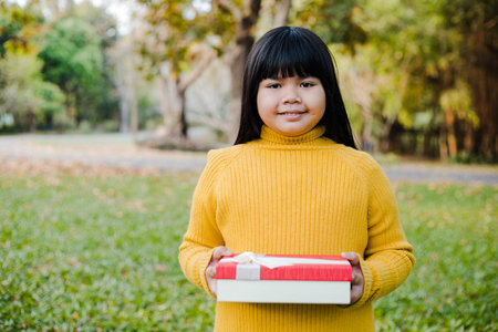 Portrait of asian little girl holding gift box in the parkの写真素材