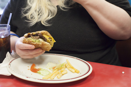 Hand holding a hamburger with a small number of French fries left on the plateの写真素材