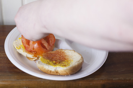 Someone adding slices of tomato to hamburger bunsの写真素材