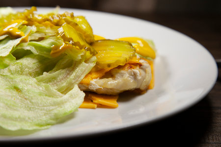 Grilled chicken breast covered in lettuce, mustard, cheese, and sliced pickesの写真素材