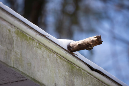 Snow and ice covering a house roof and a broken stick
