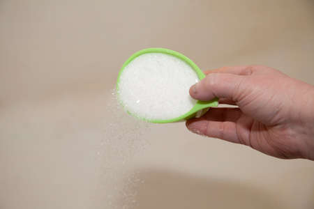 Hand pouring a cup of epsom salt into a tub