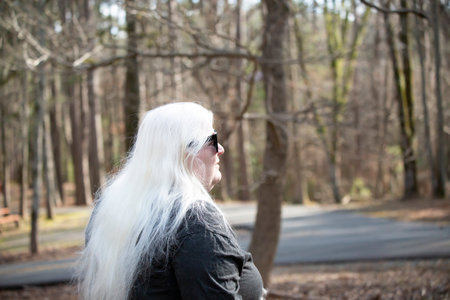 White-haired lady wearing sun shades near a forest