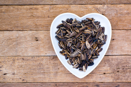 Roasted sunflower seeds in heart-shaped plate on wooden table top view from aboveの写真素材