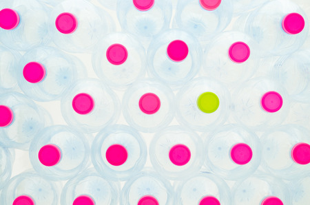 Stack of empty plastic water bottles which only one has green bottle cap and others have pink bottle capsの写真素材