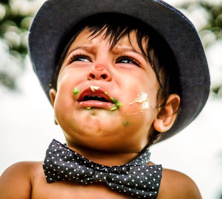 Close up outside shot of crying latino baby with cake frosting on his faceの写真素材