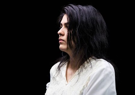 Latina teenager in white standing in front of a black background and looking to the left with a serious expression on her face.の写真素材