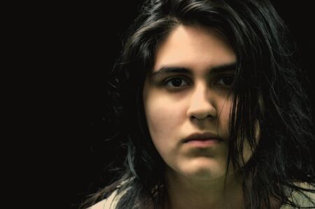 Latina teen in front of a black background and looking at the camera with a serious expression on...