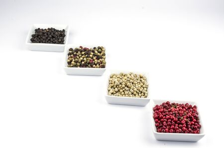 Red, white, black and sorted peppercorns on white