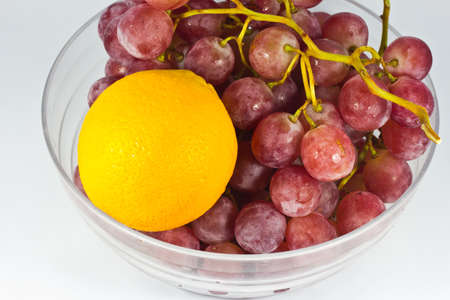Red grape and orange in white bowl on white background.