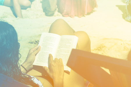 blurred background young woman reading a book while relaxing at the beach with color filterの写真素材