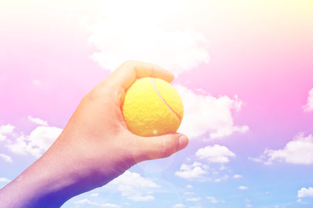 Hand holding tennis ball on blue sky backgroundの写真素材