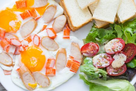 plate of fried eggs with sausage and vegetables on wooden tableの写真素材