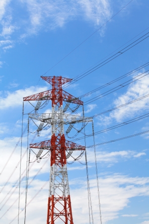 High voltage powerline and pylon against bright blue sky with white clouds の写真素材
