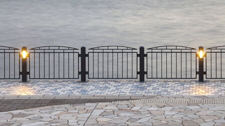 Black metal fence and floor tile beside the river at nightの写真素材