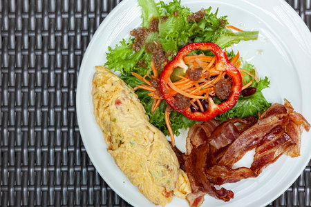 Western breakfast, scrambled eggs, bacon and fresh vegetables with tomato sauceの写真素材
