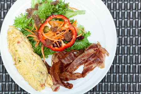 Western breakfast, scrambled eggs, bacon and fresh vegetables with tomato sauceの写真素材
