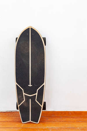 A black skateboard is placed on a white cement wall.の写真素材