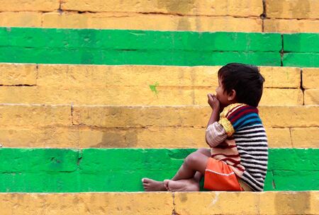 Varanasi,India - January 2,2010 :Child sitting on steps of a ghat, to protect the city from floodwaters of the river were built of stone stairs throughout the city.のeditorial素材