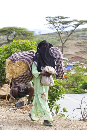 sembete, ethiopia, july 31, 2011 - women of the oromo ethnic strain on your back the goods purchased in the weekly market sembete.のeditorial素材