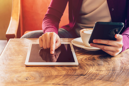 Woman hands using computer tablet and holding  smartphone in coffee shop with vintage toned.の写真素材