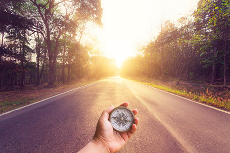 Hand holding compass on empty asphalt road and sunset.の写真素材