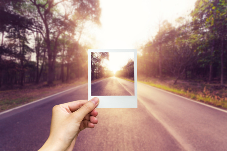 Hand holding photo frame empty asphalt road and sunset.の写真素材