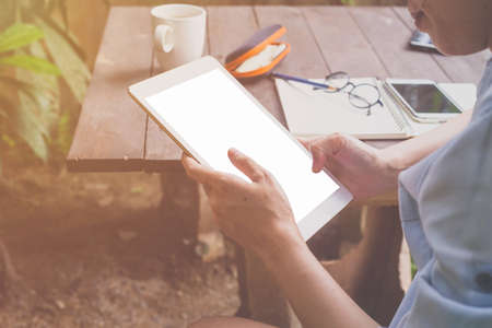 Close up hand holding and using tablet in coffee shop with vintage toned.の写真素材